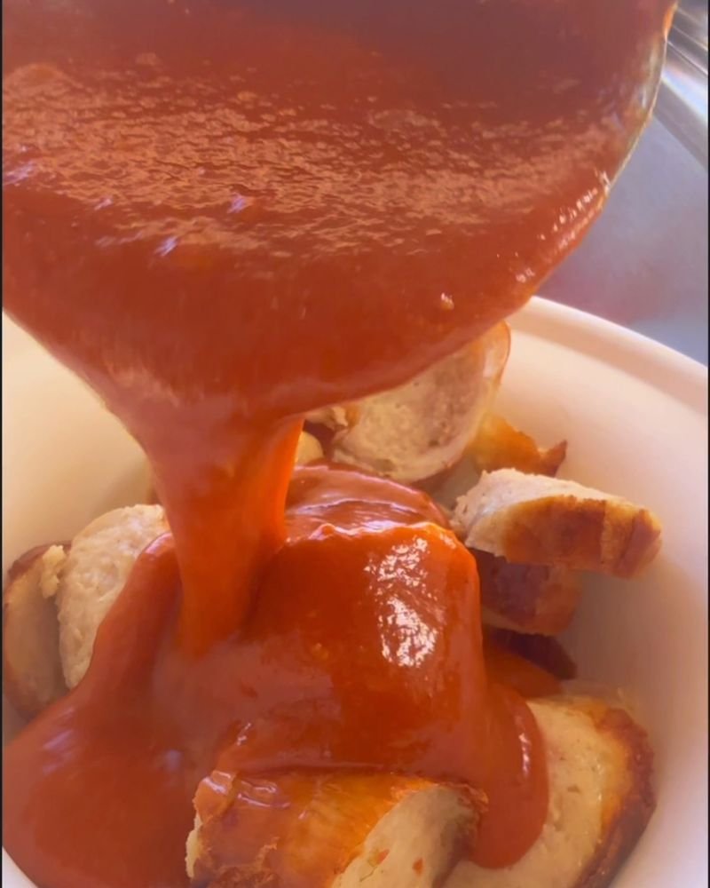 Salsa curry casera cayendo sobre una Currywurst cortada en trozos